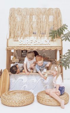 three children are sitting at a surf shack with straw baskets on the floor and one child is playing