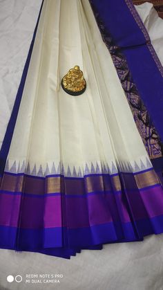 a white and blue saree with purple border on the bottom, sitting on top of a bed