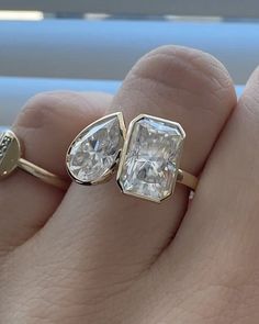 a woman's hand with two engagement rings on top of her finger, and the ring has a pear shaped diamond in it