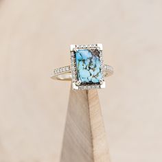 a blue and white stone ring sitting on top of a wooden block with diamonds around it