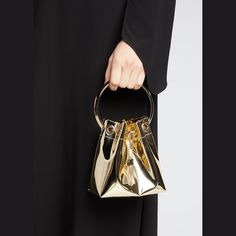 Jimmy Choo bucket bag in metallic faux leather, fabric, and brass hardware Metal ring top handle, 3.5" drop Detachable chain shoulder strap, 21.5"L Drawstring closure with chain tassels  Fabric lining  Approx. 5.9"H x 5.5"W x 3.7"D "Bon Bon" is made in Italy Luxury Gold Top Handle Bucket Bag, Luxury Gold Bucket Bag For Formal Occasions, Luxury Party Bucket Bag With Gold-tone Hardware, Gold Bucket Bag With Metal Hardware, Gold Bucket Bag With Top Handle And Gold-tone Hardware, Luxury Handheld Bucket Bag For Evening, Elegant Gold Bucket Bag For Evening, Chic Gold Bucket Bag For Evening, Elegant Gold Bucket Bag With Detachable Handle