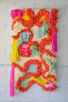 a piece of art made out of yarn and tassels hanging on a brick wall