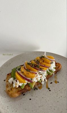 a white plate topped with an open face sandwich covered in cheese and veggies