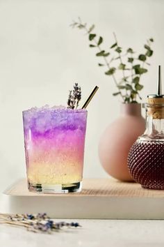 a purple and pink drink sitting on top of a wooden tray next to a vase