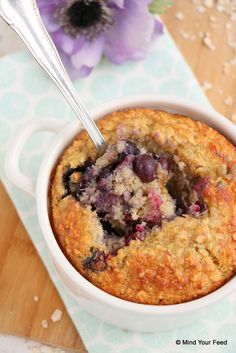 a blueberry muffin in a white bowl with a spoon next to it on a table