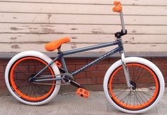 an orange and gray bike is parked in front of a brick wall with white rims