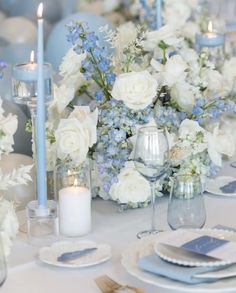 the table is set with blue and white flowers, silverware, candles and napkins