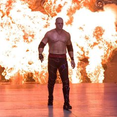 the wrestler is standing in front of a huge fire filled background with his hands on his hips