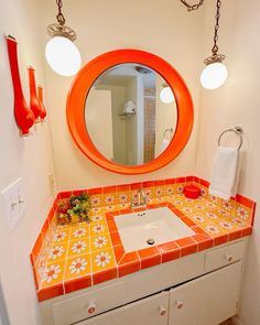 a bathroom with orange and white tile on the counter top, sink and mirror above it