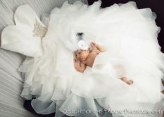 a baby in a white dress laying on top of a couch