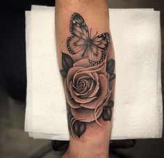 a black and white rose tattoo with a butterfly on it's arm, next to a towel