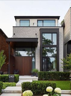 a modern house with large windows and lots of greenery in the front yard area