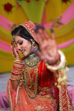 a woman in an orange and red bridal outfit holding her hand up to the camera