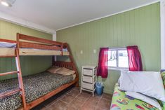 two bunk beds in a room with green walls and brown tile flooring on the ground