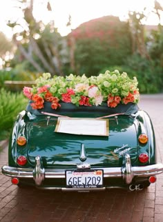 an old green car with flowers in the back seat and a sign on the trunk