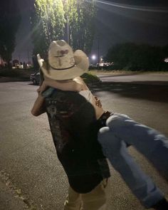 two people in cowboy hats are walking down the street at night with their arms around each other