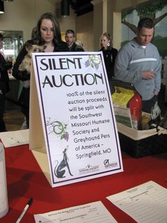 a sign that says silent auction sitting on top of a table with people standing around it