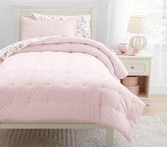 a bed with pink comforter and pillows in a white room next to a window