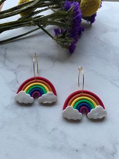 two rainbows are hanging from the side of a pair of gold hoop earrings on a marble surface