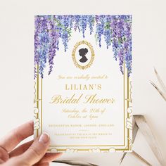 a person holding up a wedding card with purple flowers on the front and back,