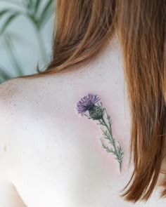 the back of a woman's shoulder with a small flower tattoo on her left side