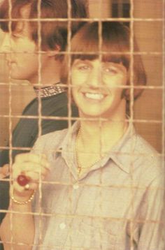 a woman holding an apple in front of a man behind a wire mesh fence smiling at the camera