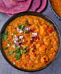 two bowls filled with red lentula soup and garnished with cilantro