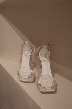 a pair of white high heeled shoes sitting on top of a table next to a wall