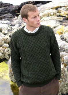 a man standing in front of some rocks wearing a green sweater