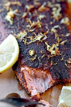 a piece of meat on a cutting board with lemon wedges and seasoning next to it