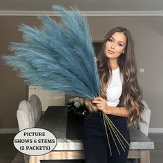 a woman standing in front of a dining room table holding a bunch of blue feathers