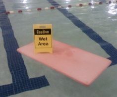 a caution sign sitting on top of a pink mat in a swimming pool with blue and white tiles