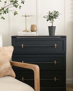 a black chest of drawers sitting next to a white chair and a potted plant