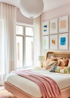 a bedroom with pink walls and pictures on the wall above the bed, in front of a large window