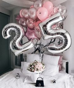 the number twenty five balloon bouquet is displayed on a bed with white sheets and pillows