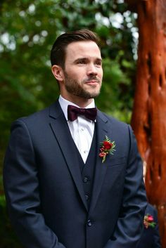 a man wearing a suit and bow tie standing in front of a wooden tree trunk