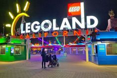 two people standing in front of the entrance to legoland california at night with lights on