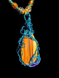 Embrace the grounding and protective energies of Tiger's Eye with this stunning handmade pendant. This unique piece features a polished Tiger's Eye stone, known for its beautiful bands of golden brown and vibrant hues. The stone is intricately wrapped in teal wire, adding an artistic and modern touch to the natural beauty of the gemstone. The pendant is complemented by a meticulously beaded necklace, showcasing a harmonious blend of amber, teal, and clear beads that catch the light beautifully. Earthy Orange Jewelry As Gift, Amber Necklace Hand Wrapped For Healing, Hand Wrapped Amber Necklace For Healing, Earthy Orange Jewelry Gift, Earthy Handmade Crystal Necklaces As Gifts, Healing Wire Wrapped Pendant Beaded Necklaces, Handmade Amber Beaded Necklace For Healing, Amber Hand Wrapped Necklace For Healing, Multicolor Hand Wrapped Necklaces For Healing