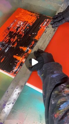 someone using a large pair of scissors to paint an orange piece of art with black and red colors