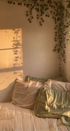 an unmade bed with white sheets and plants growing on the wall above it, in front of a window