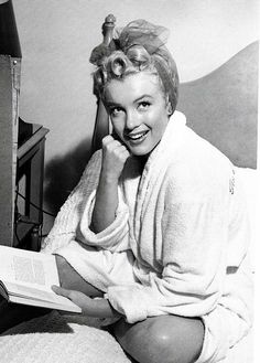 a black and white photo of a woman sitting on a bed with a book in her hand