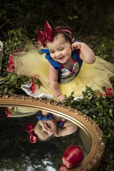 a baby girl in a snow princess costume looking at herself in the mirror with her reflection