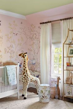 a giraffe standing next to a baby crib in a room with pink walls