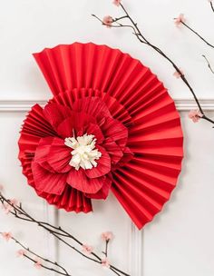 a red paper fan sitting on top of a white wall next to branches with pink flowers