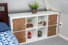 a white shelf with books and plants on it next to a blue bed in a bedroom