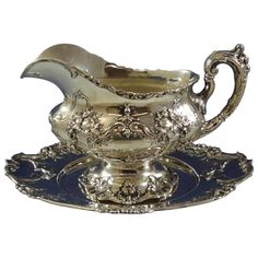 a silver pitcher and saucer sitting on top of a blue plate with an ornate design