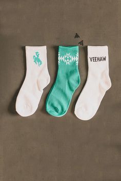 Three pairs of SOCK EM SILLY *CRISP western socks from 2 Fly are displayed on a flat surface. The left pair is white with a turquoise horse graphic, the middle pair is green with a white geometric pattern, and the right pair is white with the word YEEHAW printed in black text. This 3 pack comes in one size that fits most. Silly Socks, Western Vibes, Foot Socks, Sock Game, Kids Sale, Top Graphic Tees, Boot Socks, Country Western, Kids Socks