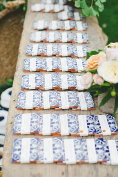 blue and white tiles laid out on a wooden table with flowers in vases next to them