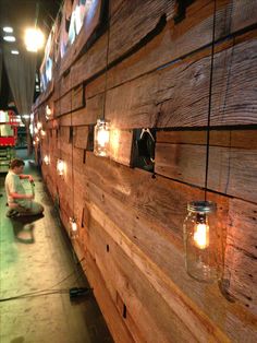 a man sitting on the floor next to a wooden wall with mason jars hanging from it