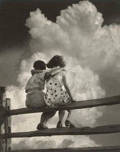 two children sitting on a fence looking at the clouds